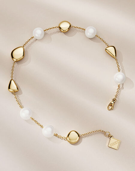 Birks Pebble yellow gold and pearl bracelet on a beige background.