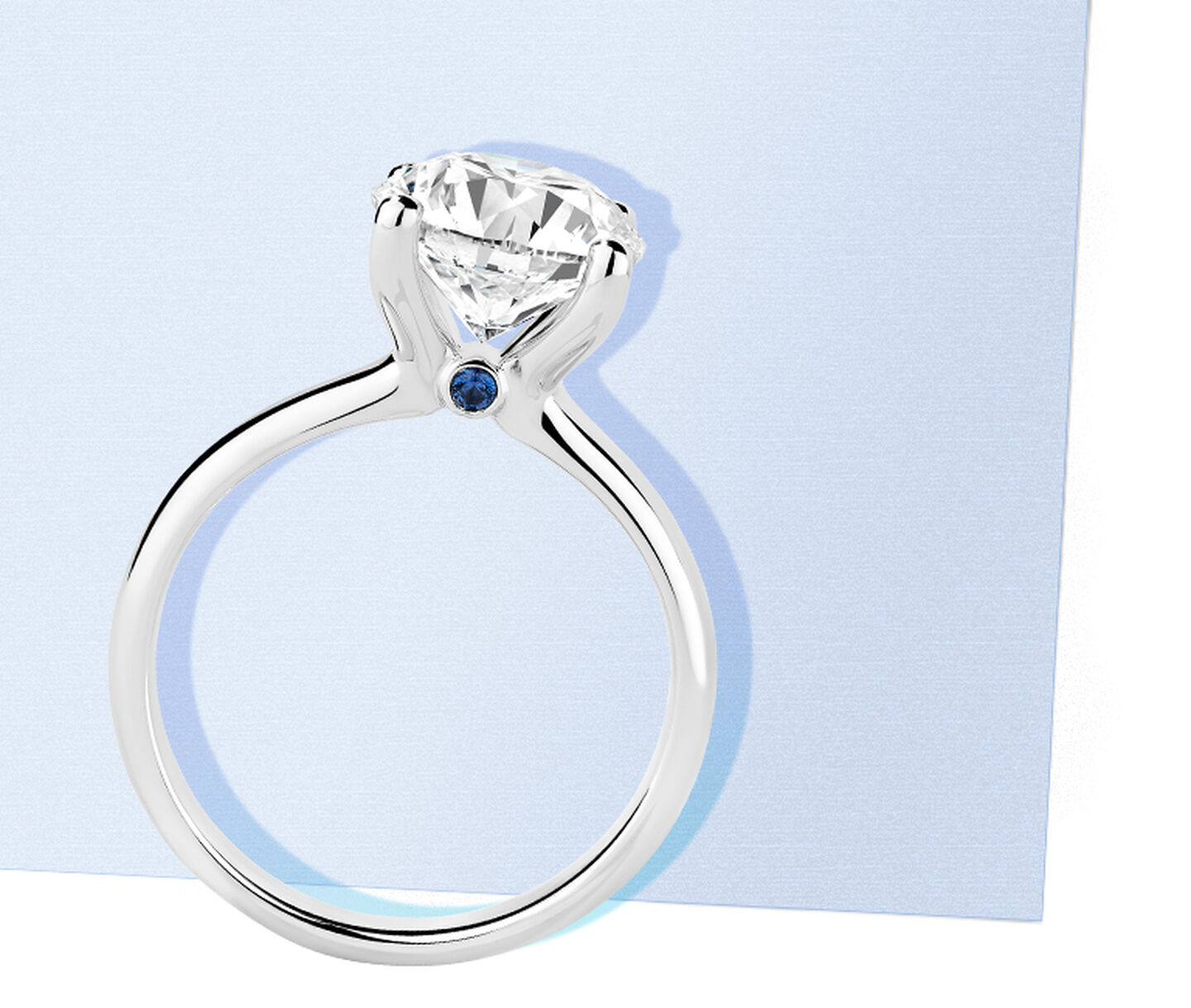 Birks Blue Round Diamond Solitaire Engagement Ring with Sapphire Accent on a blue background.