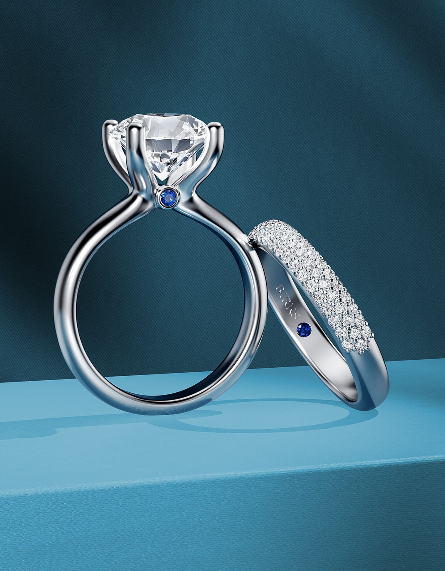 Bague de fiançailles Birks Blue avec une alliance de mariage sur un fond bleu.