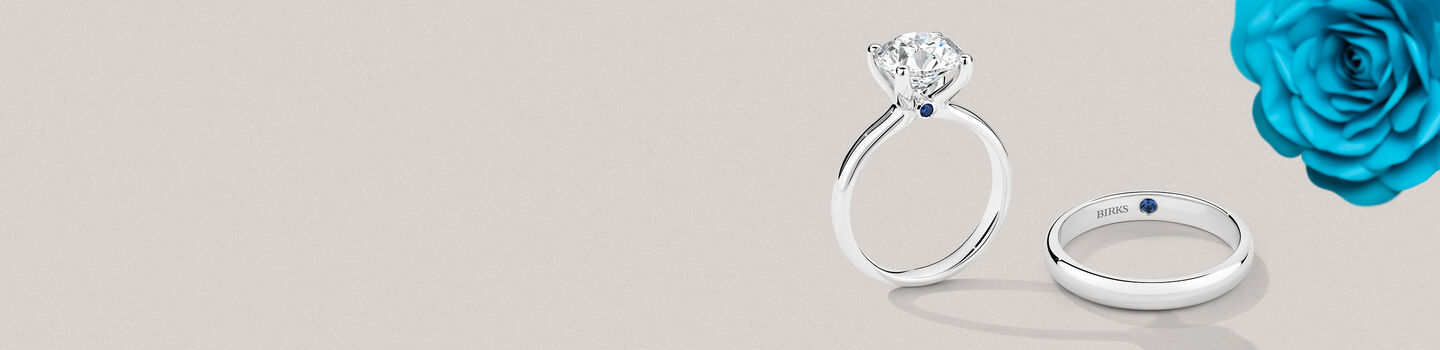 Bague de fiançailles et alliance en diamant Birks Blue à côté d'une rose bleue