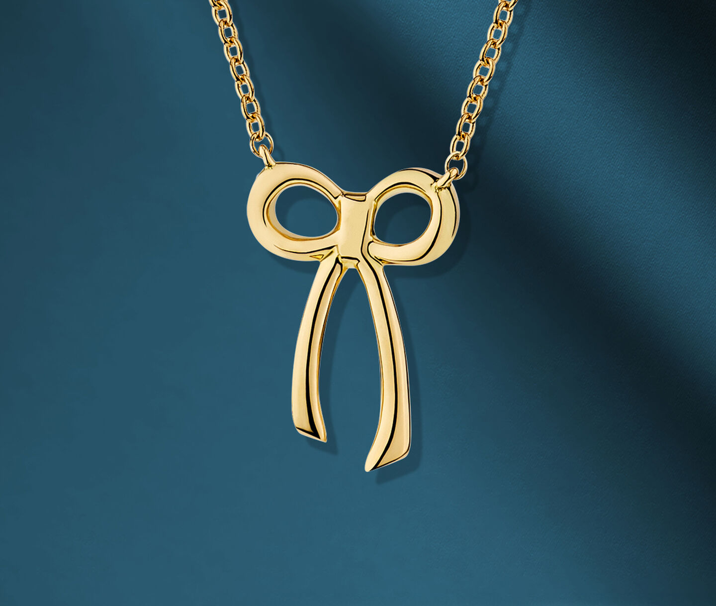 Birks Essentials yellow gold bow necklace on a blue background.