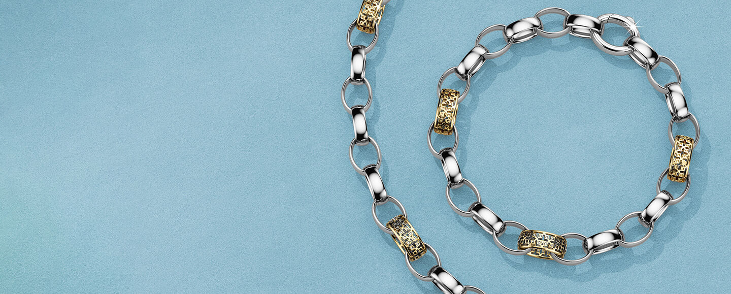 Birks Dare to Dream silver and gold necklace and bracelet on a blue background.
