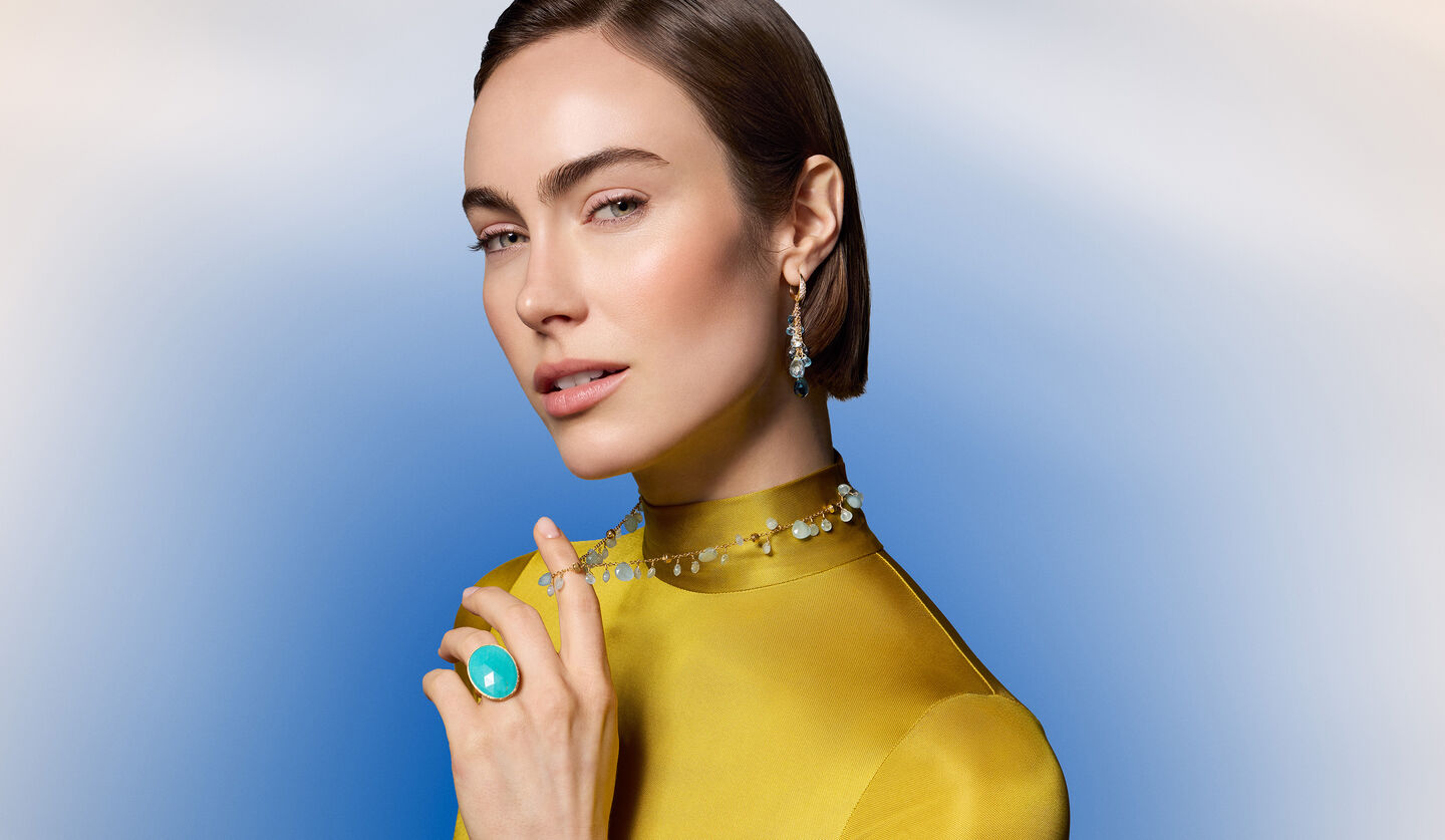 A woman wearing Marco Bicego gemstone jewellery on a blue background.