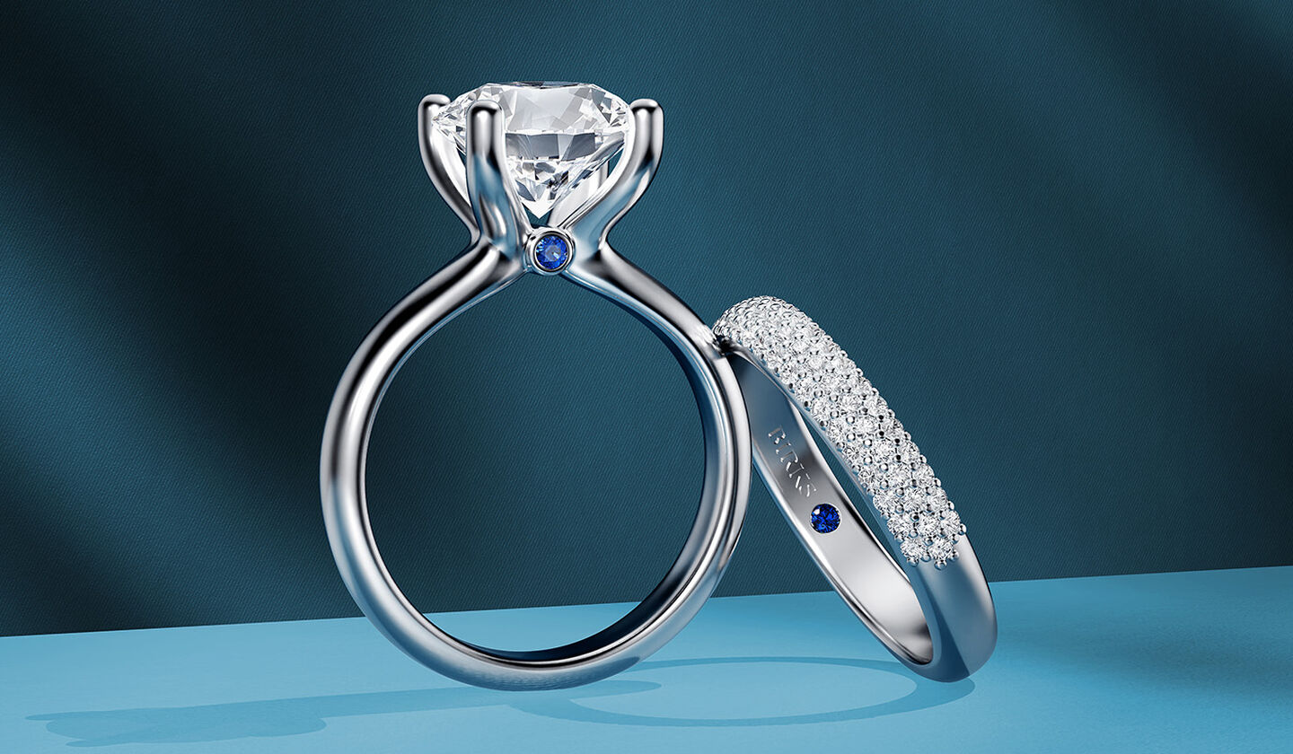 Birks Blue round solitaire diamond engagement ring with a wedding band on a blue background.