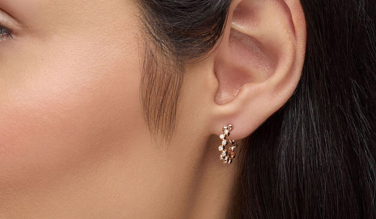 Une femme porte les boucles d'oreilles Birks Iconic Splash en or rose et diamants.