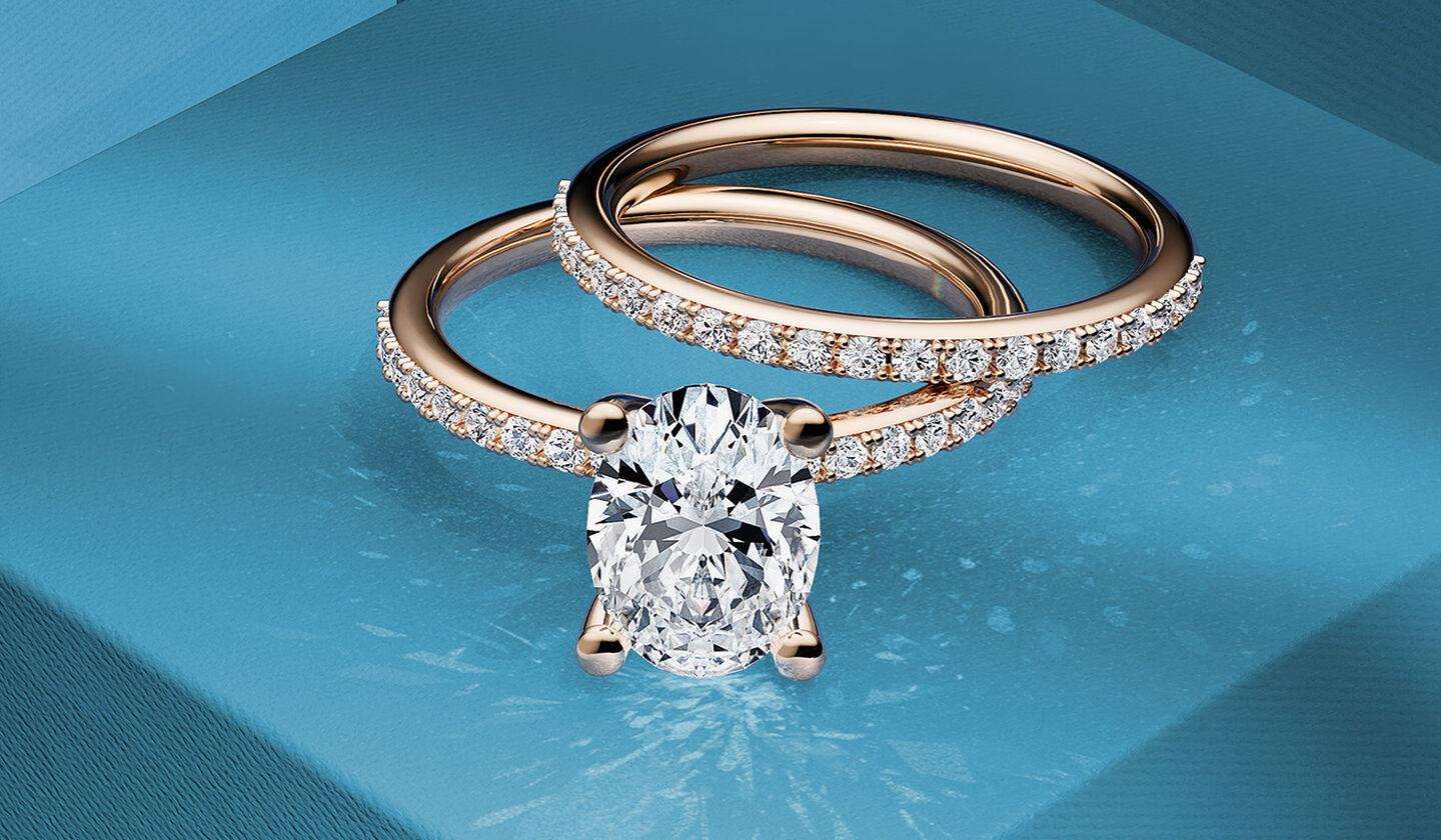 Birks Rosée du Matin oval shaped diamond engagement ring with a wedding band on a blue background.