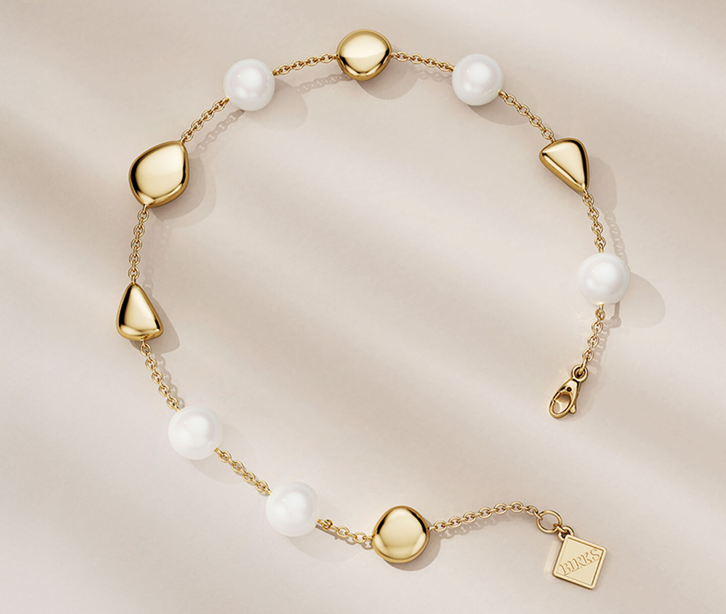 Birks Pebble yellow gold and pearl bracelet on a beige background.