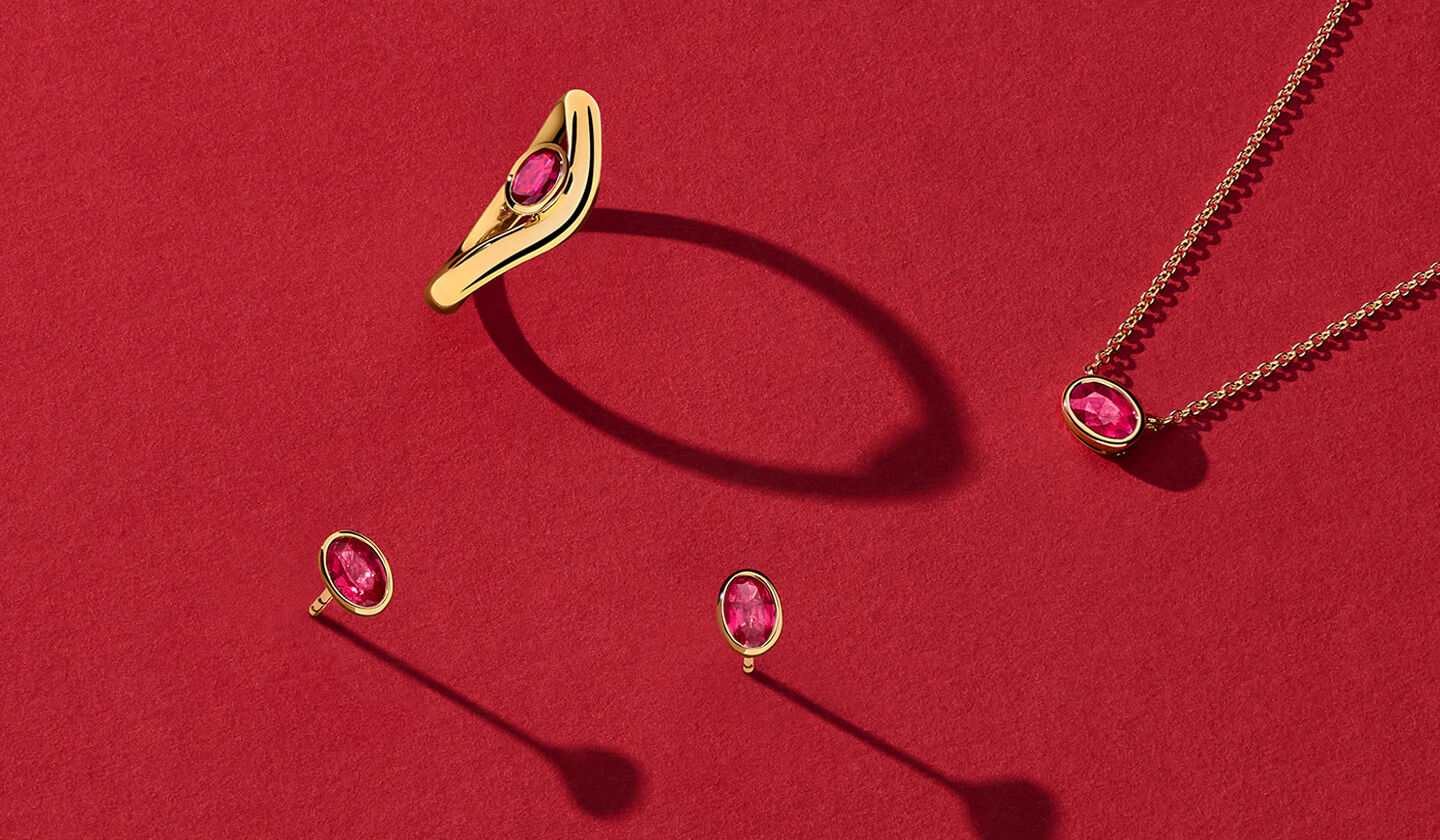 Birks Essentials yellow gold and ruby jewellery on a red background.