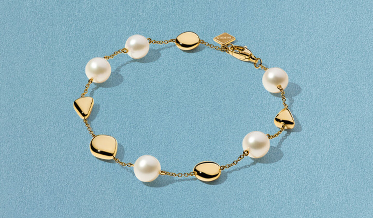 Birks Pebble gold and pearl bracelet on a blue background.