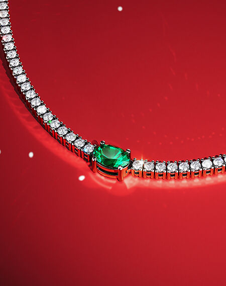 Birks Essentials emerald and diamond necklace on a red background.