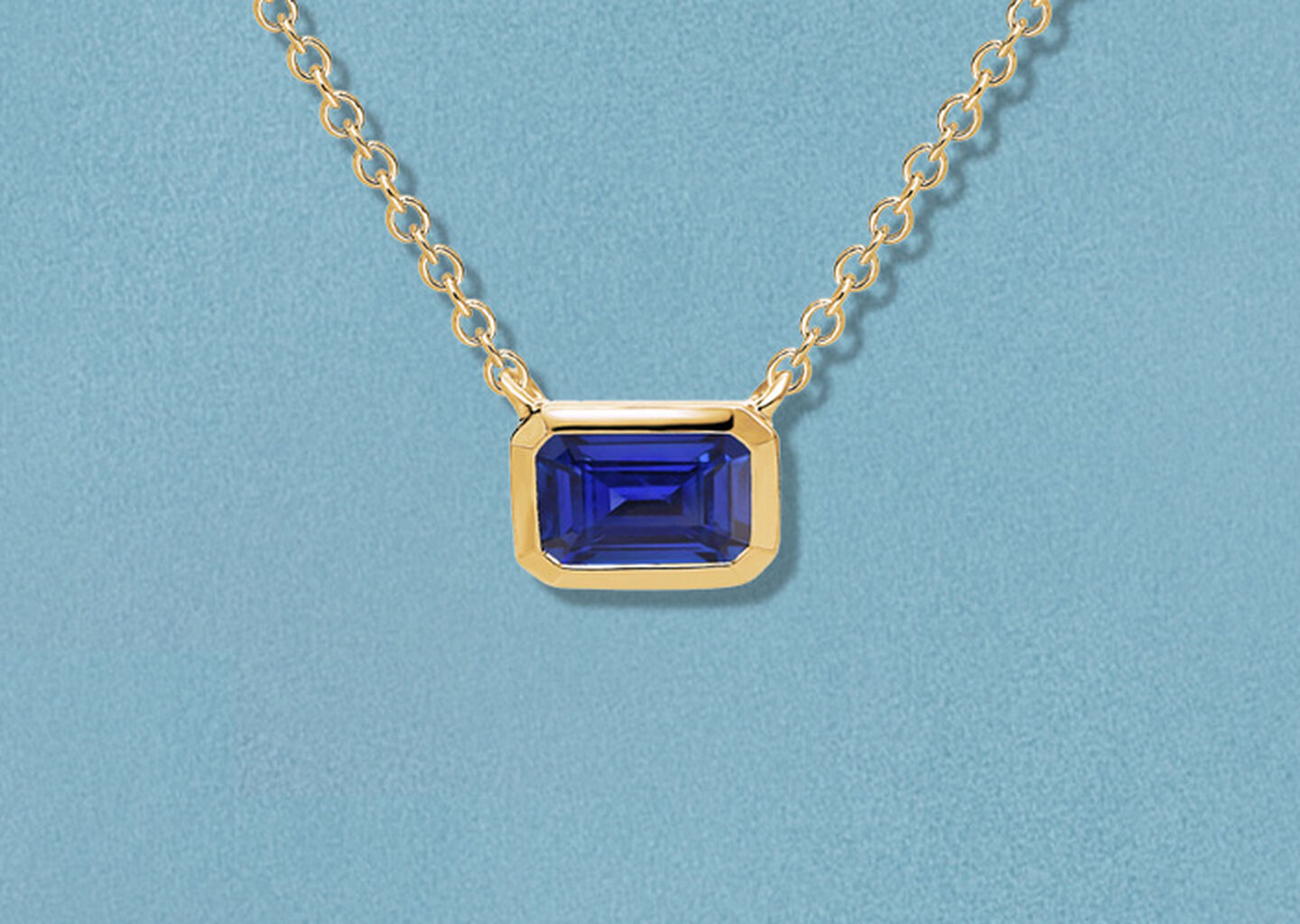 Birks Essentiels collier en or jaune avec saphir sur fond bleu.