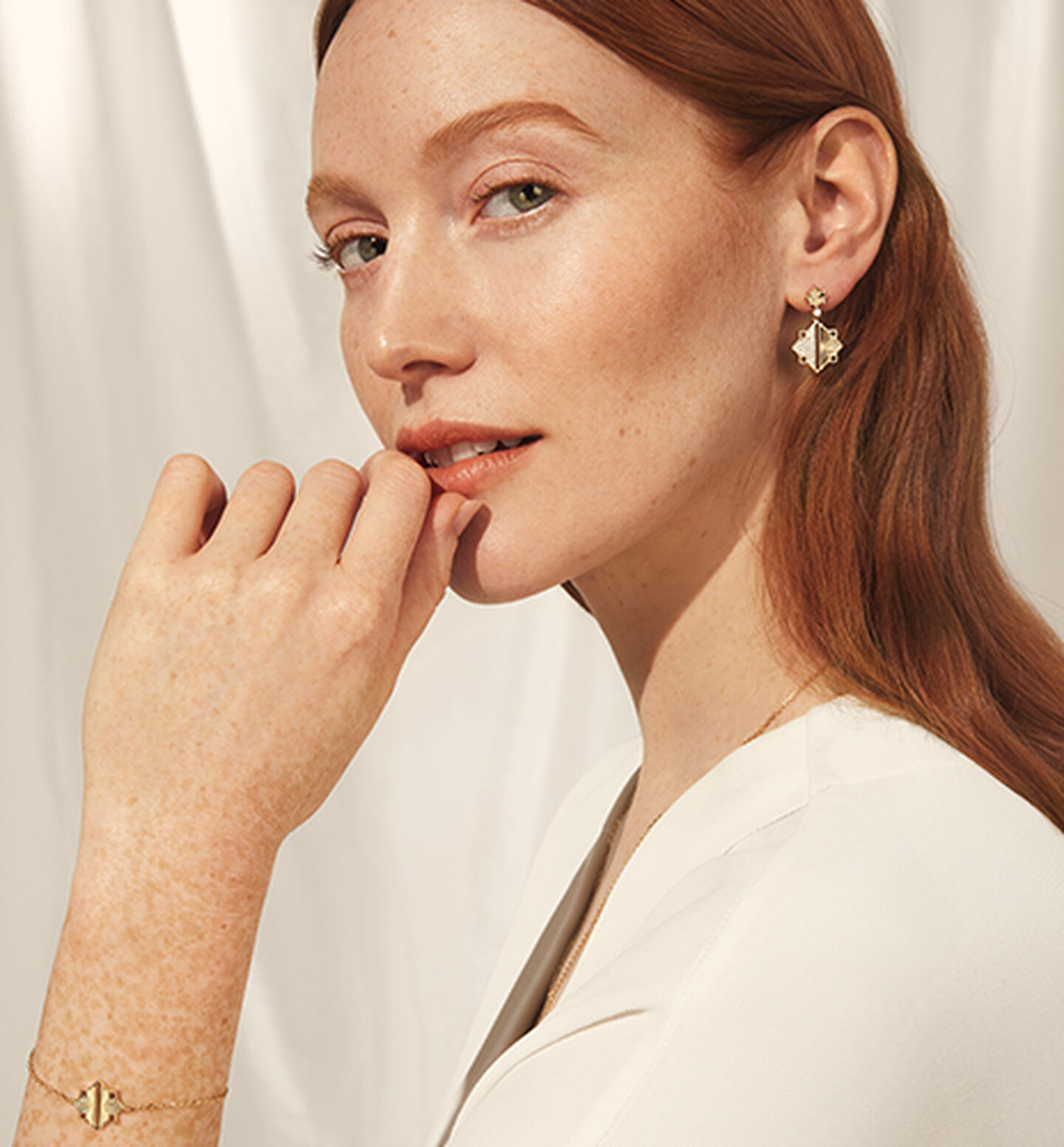 A woman wearing Birks Muse yellow gold drop earrings on a beige background.