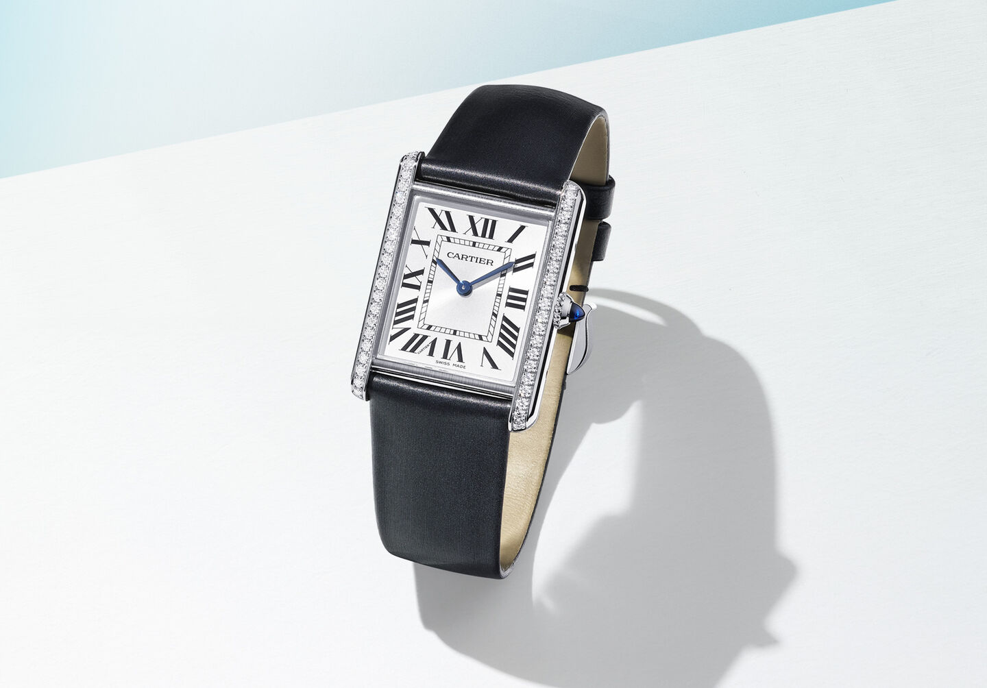 Une montre Tank Must de Cartier sur un fond bleu.