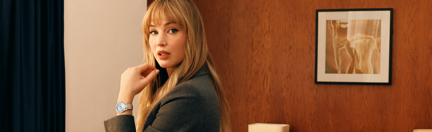 Jennifer Lawrence wearing a Longines Master Collection watch with an elegant blazer in a refined interior setting.