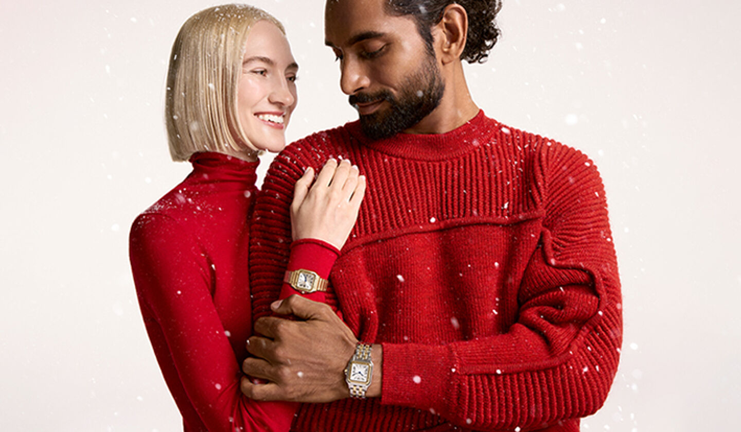  A couple wearing a red sweater and Cartier panthere watches on a beige snowy background.