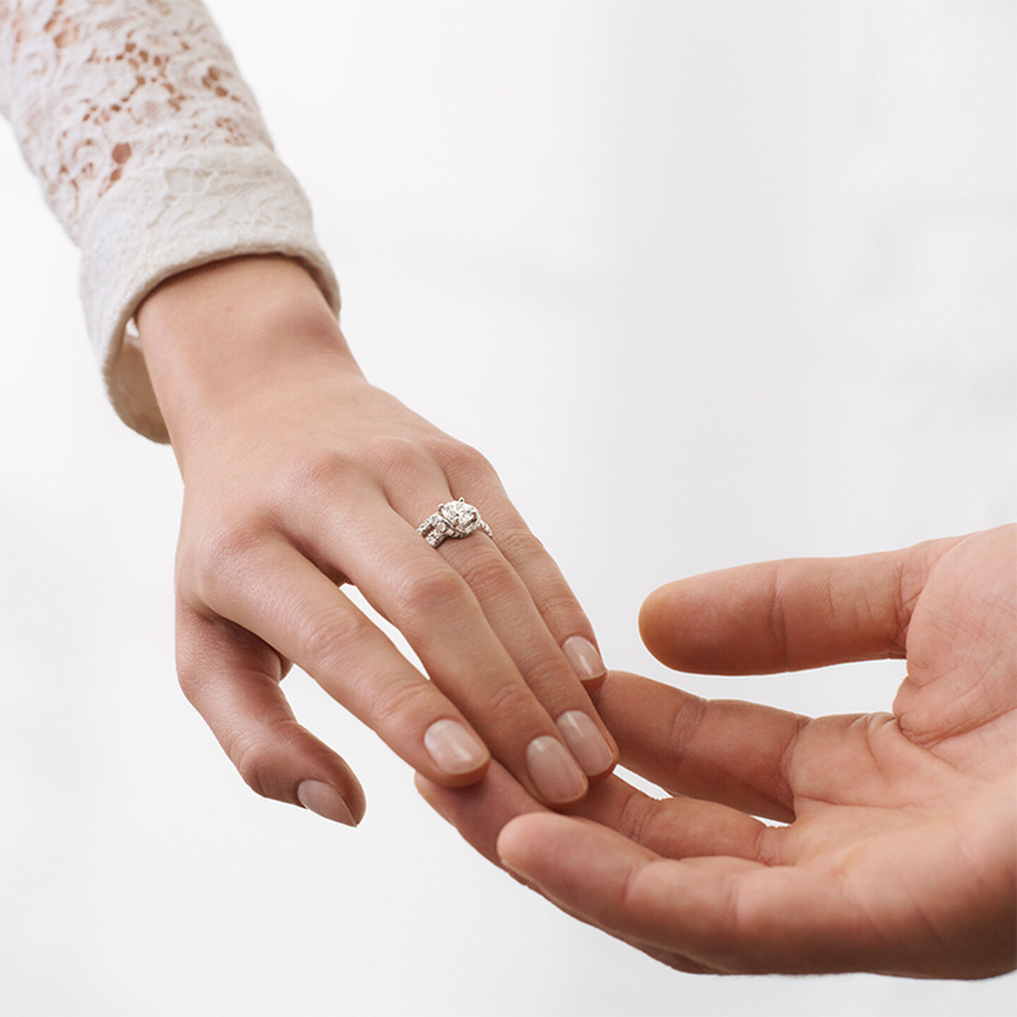 Photo de mains : l'une porte une bague de fiançailles Chaumet sur fond blanc