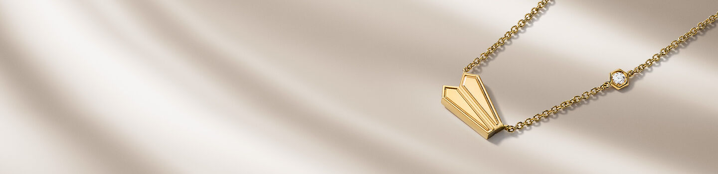 Birks Beekeeper yellow gold necklace on a beige background.