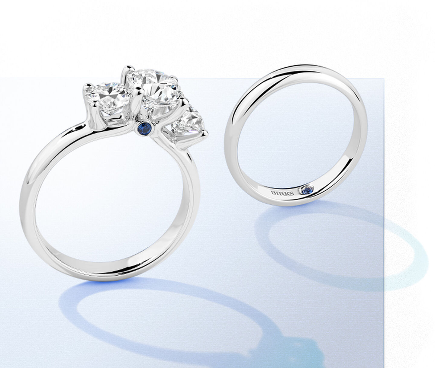 A white gold wedding band stands next to a diamond engagement ring