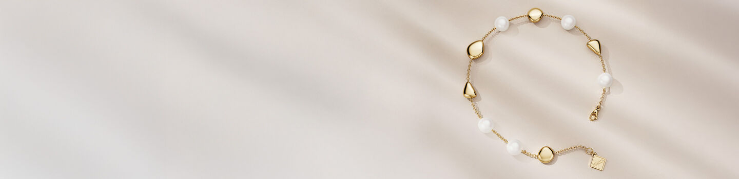 Bracelet Birks Pebble avec perles en or jaune sur un fond beige.