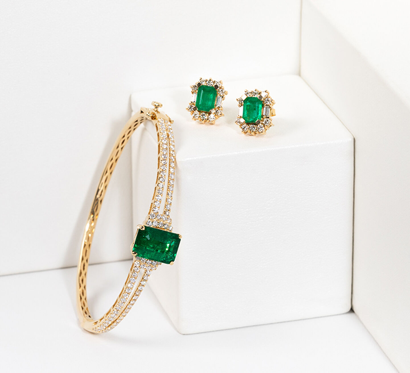 Gold and diamond bracelet with an emerald stone beside matching earrings