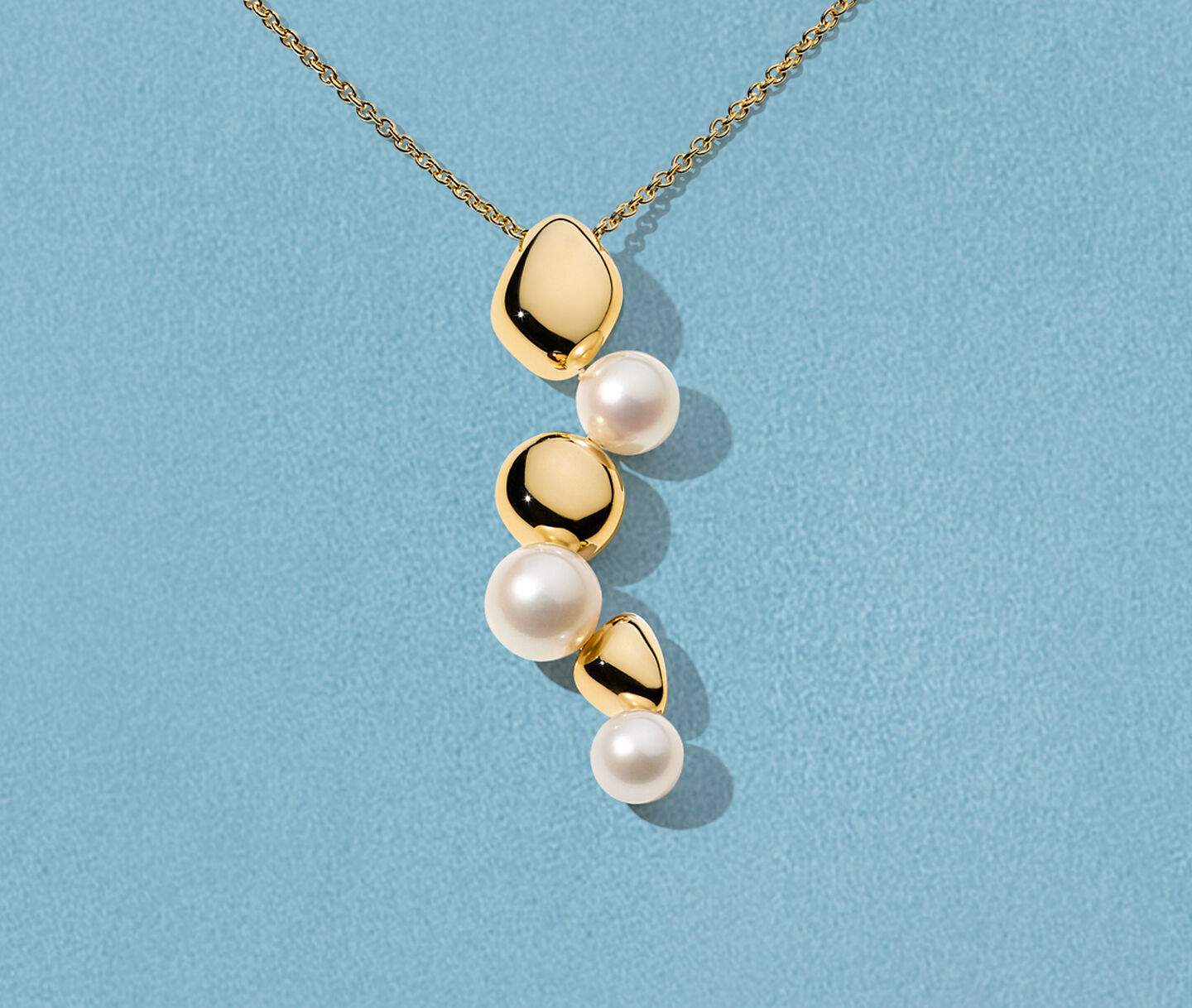Birks Pebble gold and pearl necklace on a blue background.