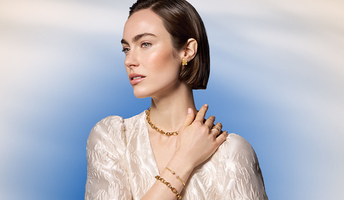 Une femme porte les bijoux en or jaune de Birks et Roberto Coin.