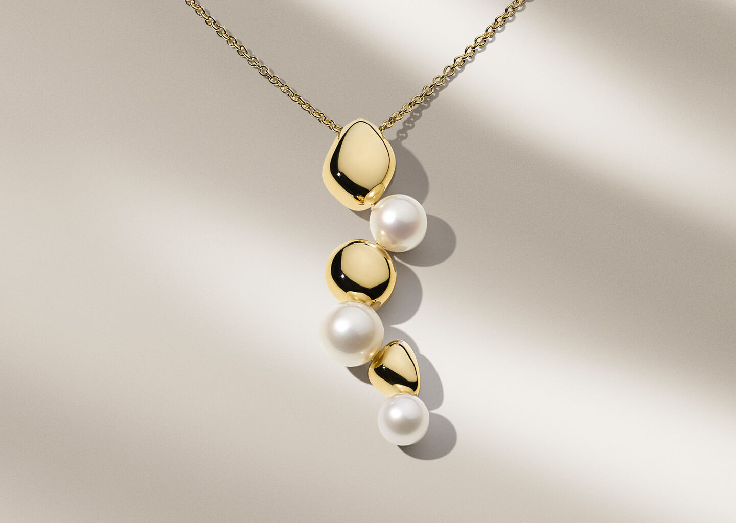 Birks Pebble gold and pearl necklace on a beige background.