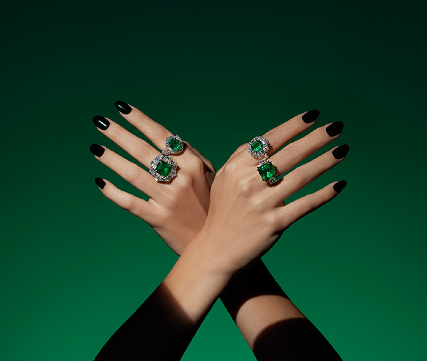 Une main de femme portant les bagues haute joallerie avec émeraude de Maison Birks sur un fond vert.