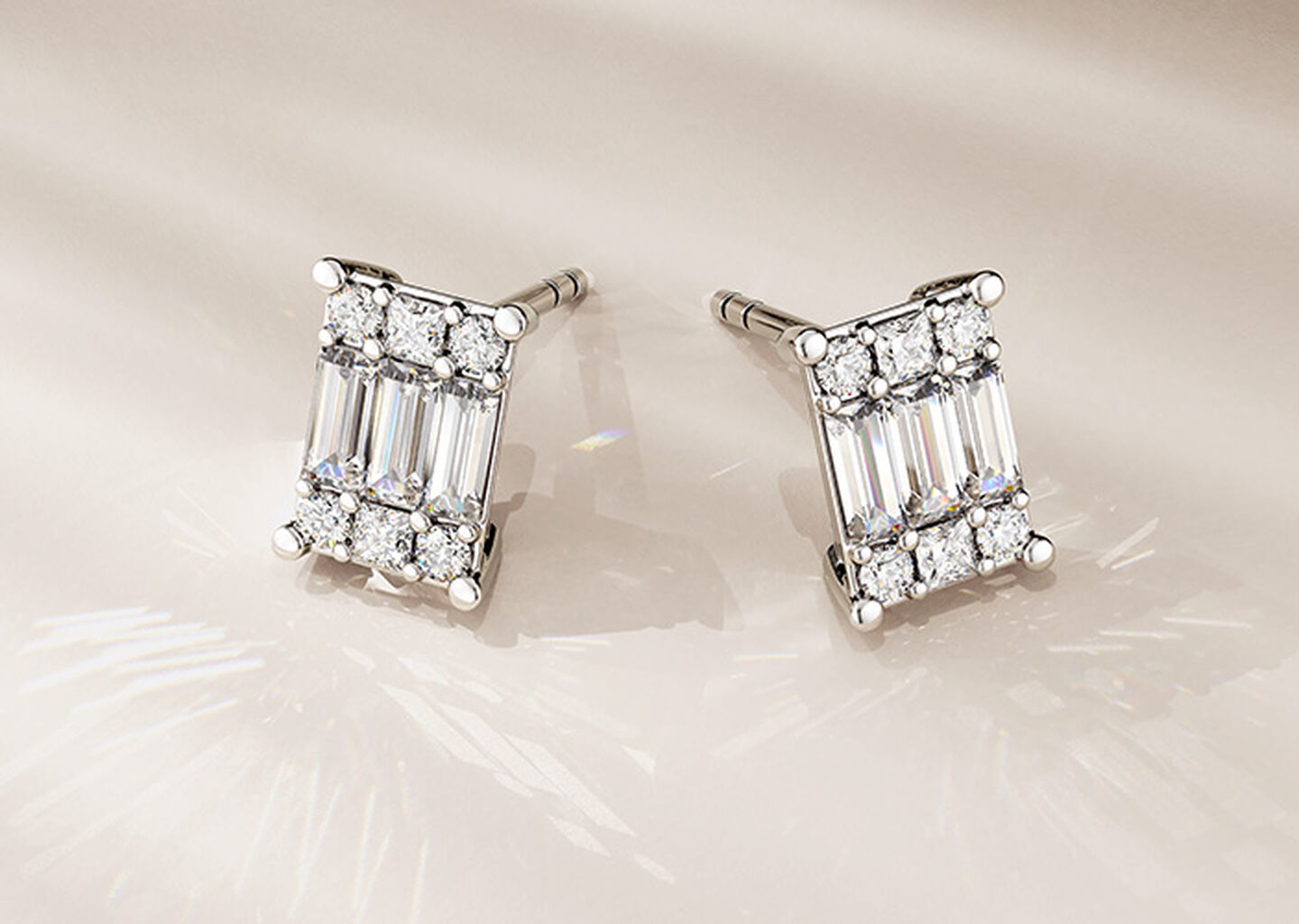 Boucles d'oreilles Birks Essentiels avec diamants sur un fond beige.