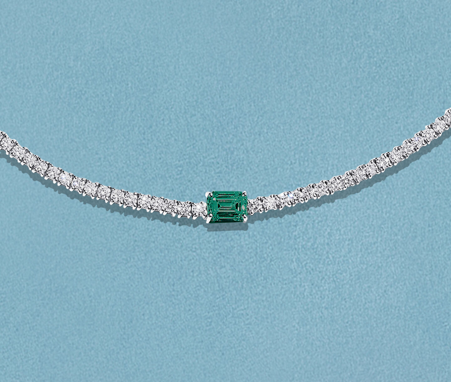 Collier Birks Essentiels avec &eacute;meraude et diamants sur un fond bleu.