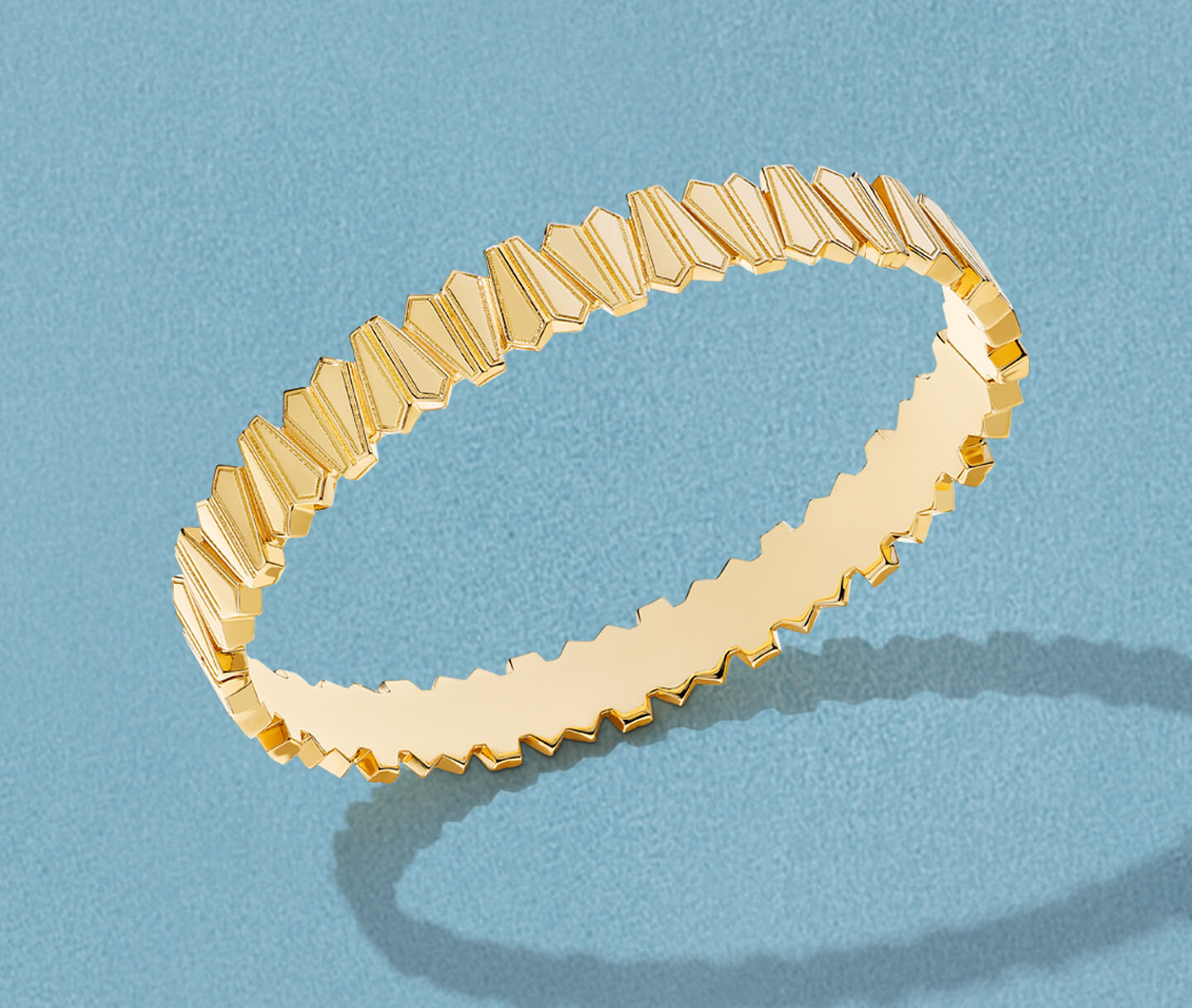 Birks Beekeeper yellow gold bangle bracelet on a blue background.