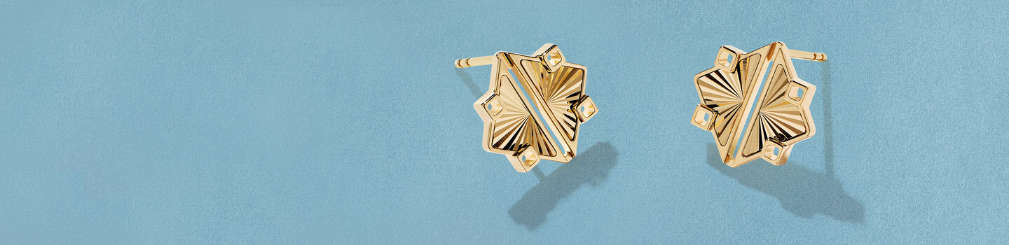 Boucles d'oreilles Birks Muse guilloch&eacute; en or jaune sur un fond bleu.