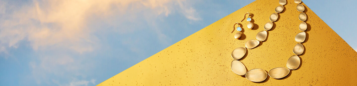 Marco Bicego lunaria necklace and earring on a orange background.