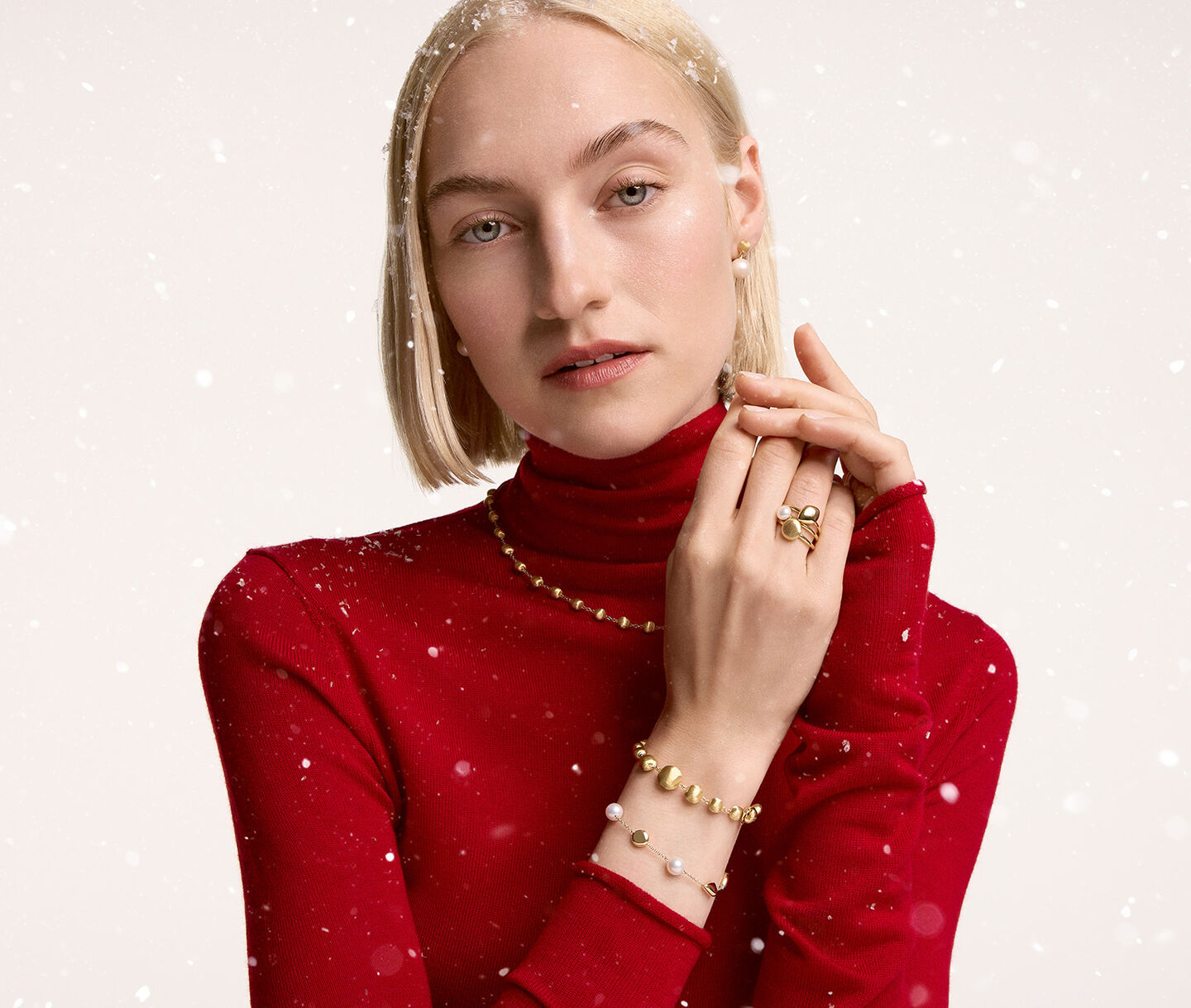 A woman wearing: Birks yellow pebble ring and bracelet, Marco bicego africa necklace and bracelet on a beige snowy background.