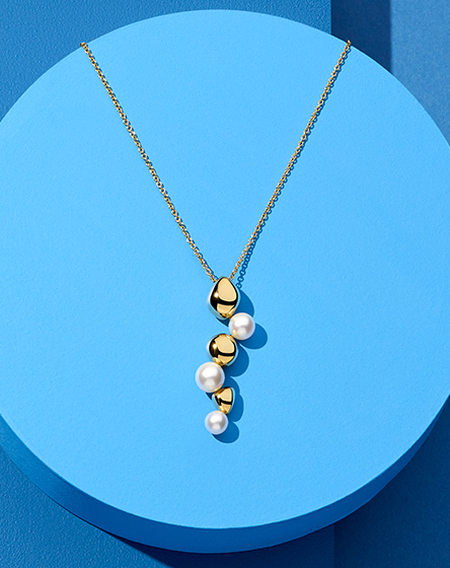 Birks Pebble yellow gold and pearl necklace on a blue background.