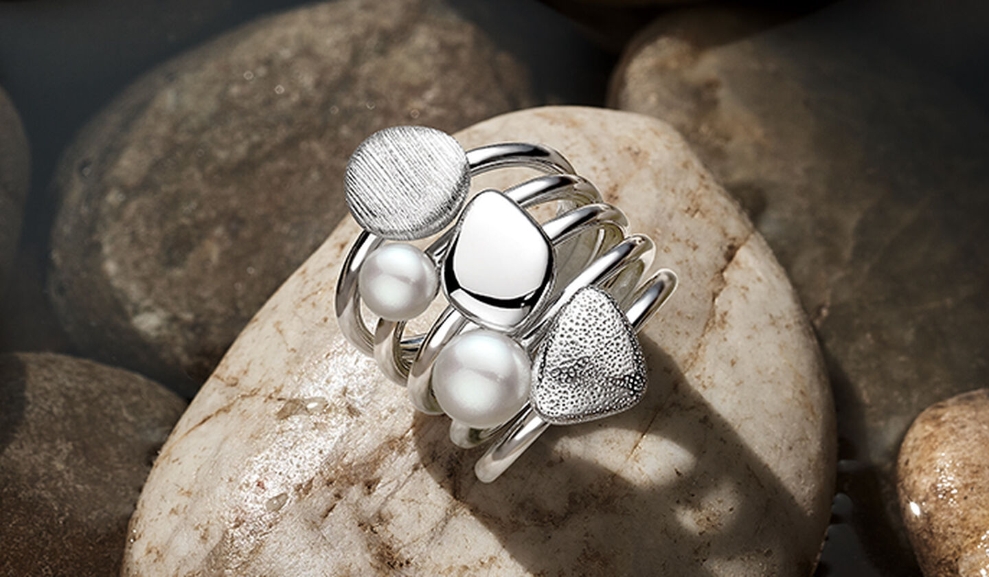 Birks silver rock and pearl stackable rings on a rock- brown background