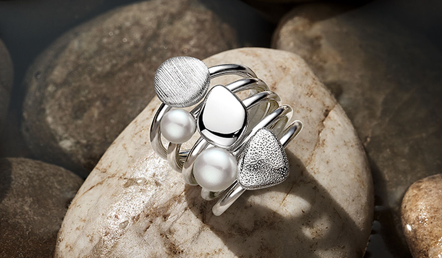 Bagues empilables Birks en argent, en pierre et en perles, sur fond brun rocheux