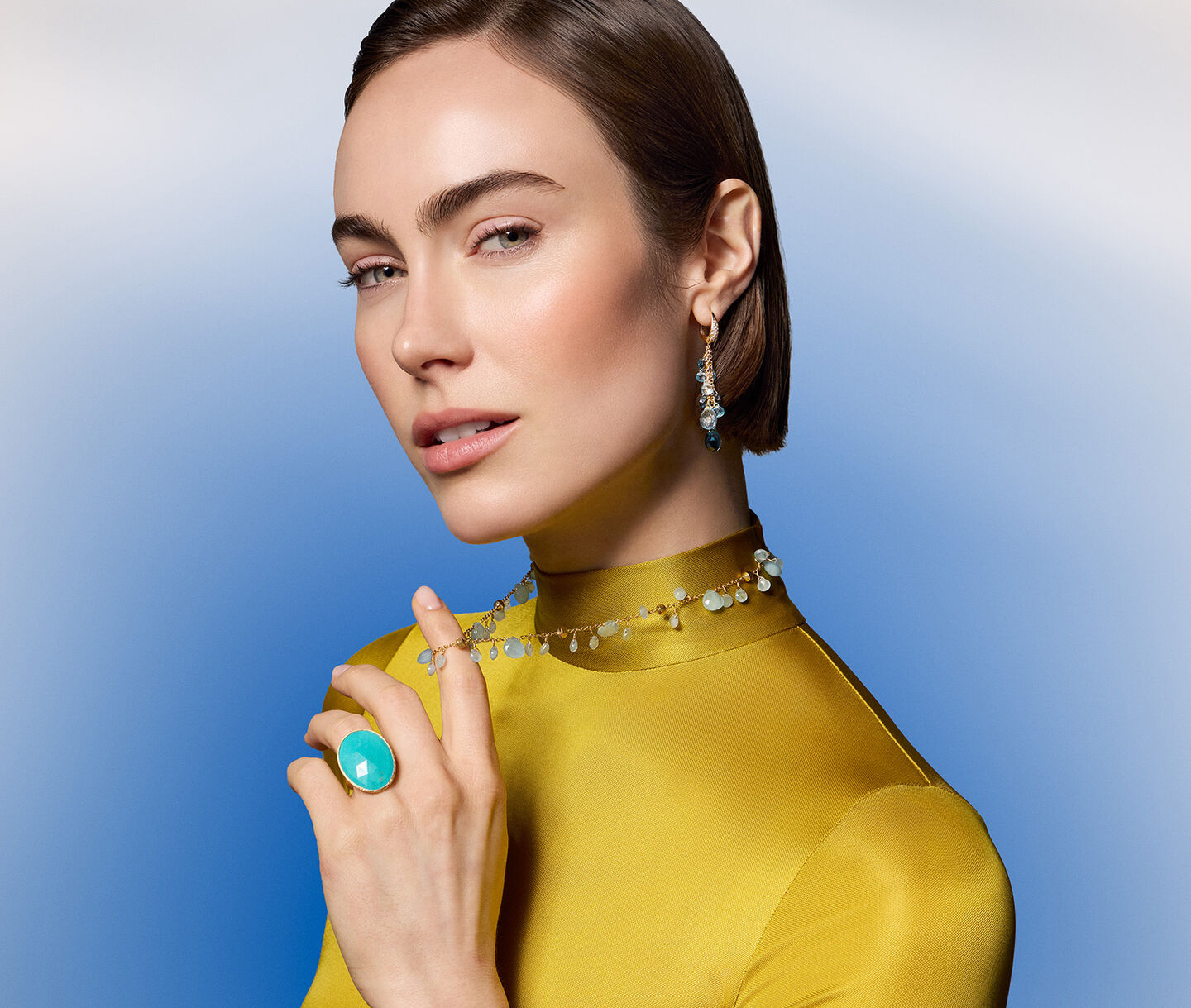 A woman wearing Marco Bicego gemstone jewellery on a blue background.