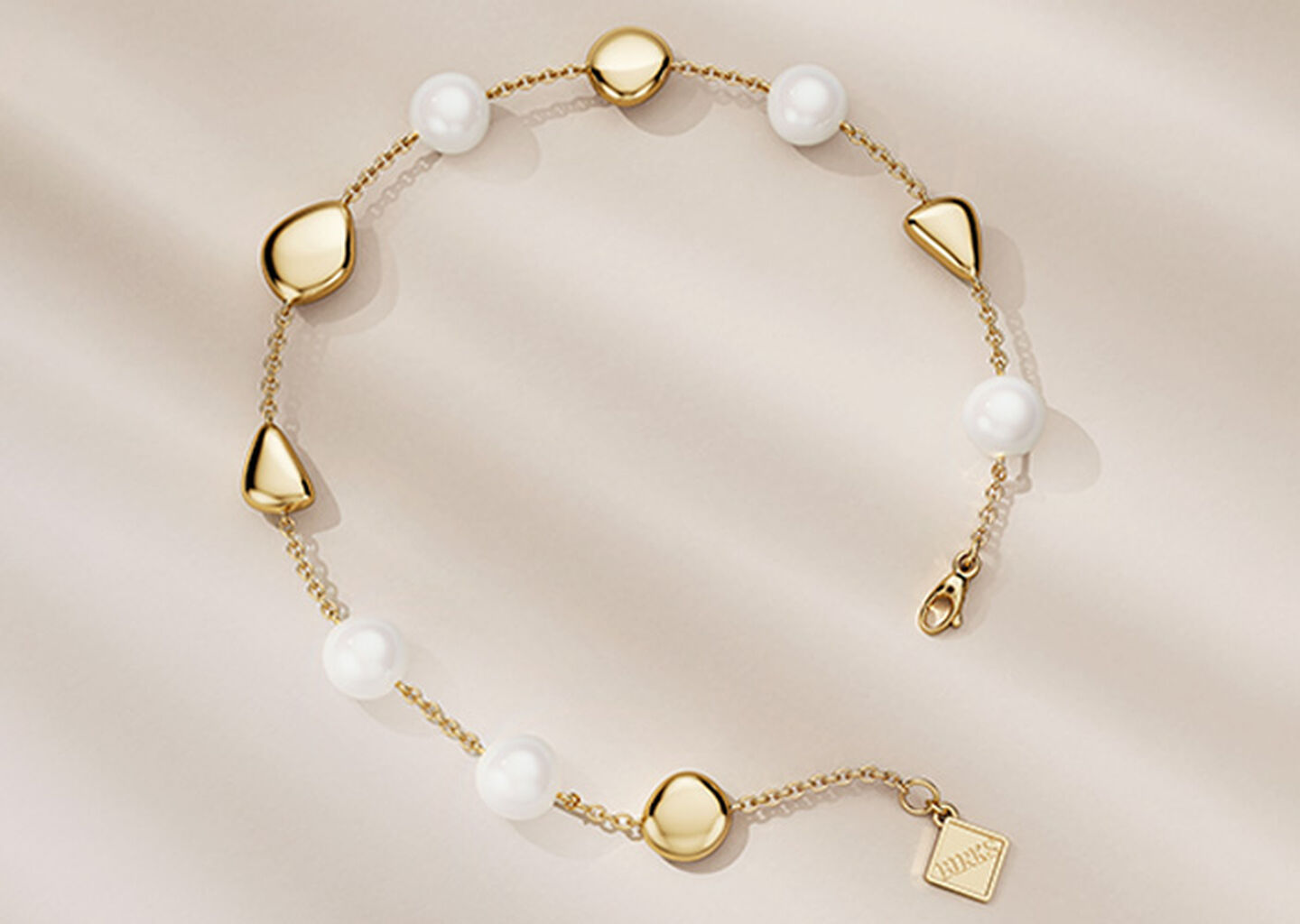 Birks Pebble yellow gold and pearl bracelet on a beige background.