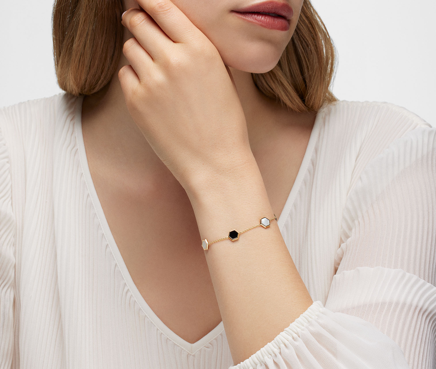 Une femme porte la bracelet Birks Bee Chic en or jaune avec onyx et nacre.
