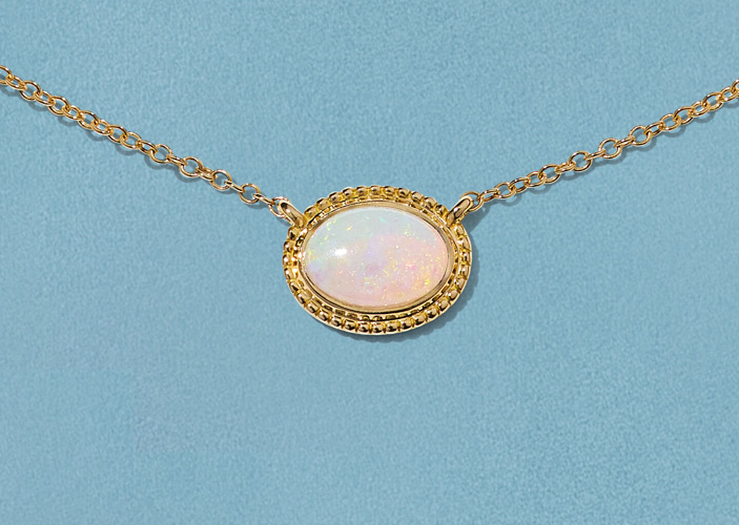 Birks Essentiels collier en or jaune avec opale sur fond bleu.