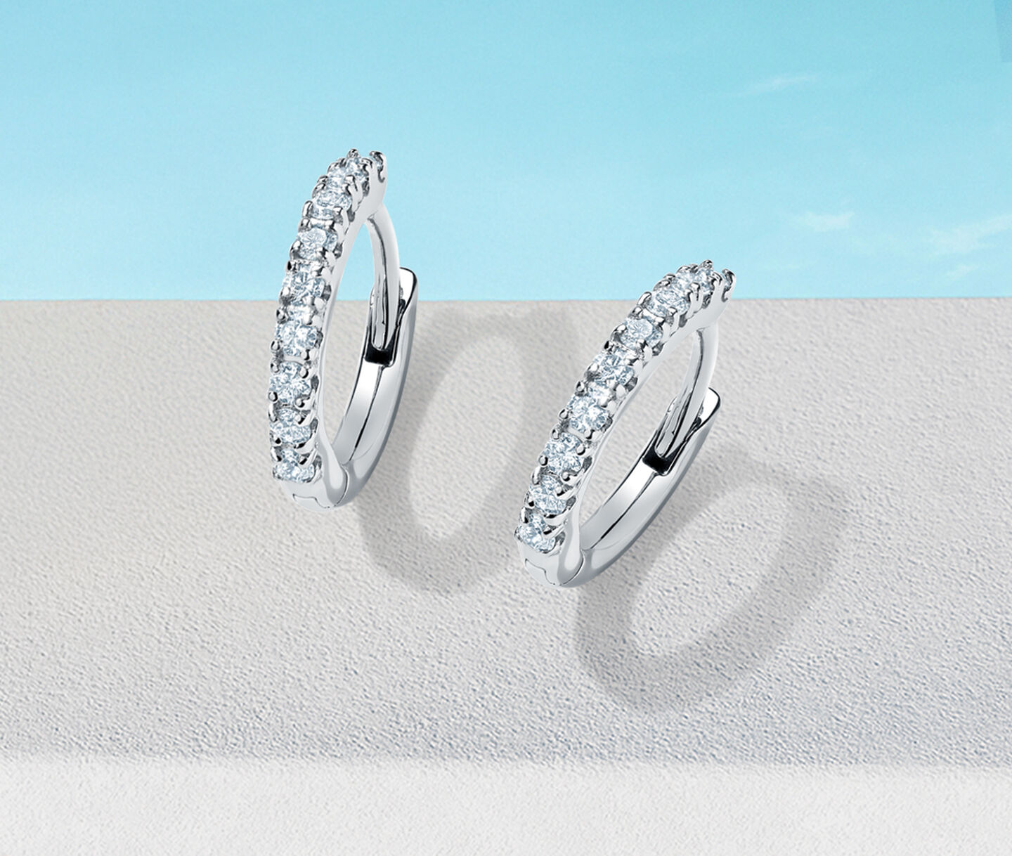 Birks Iconic Rosee du Matin diamond hoop earrings on a blue background.