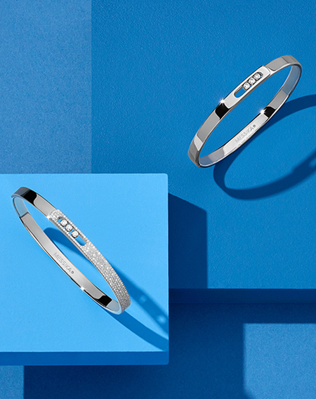 Messika diamond and white gold bangle bracelets on a blue geometric background.
