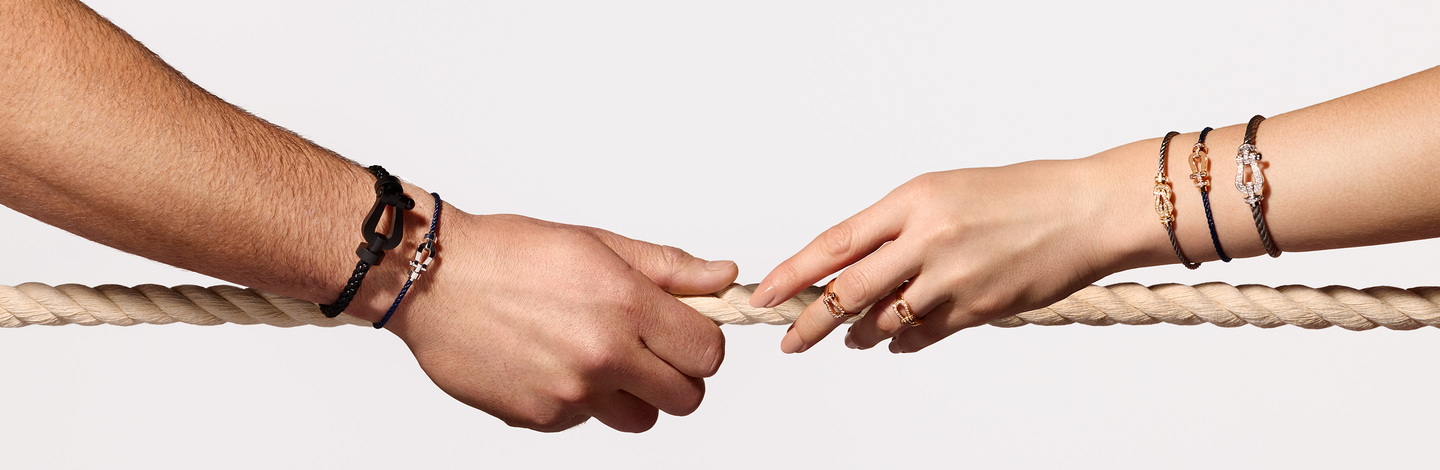 Hand model wearing FRED force 10 and chance infinie bracelets and rings on a cream background.