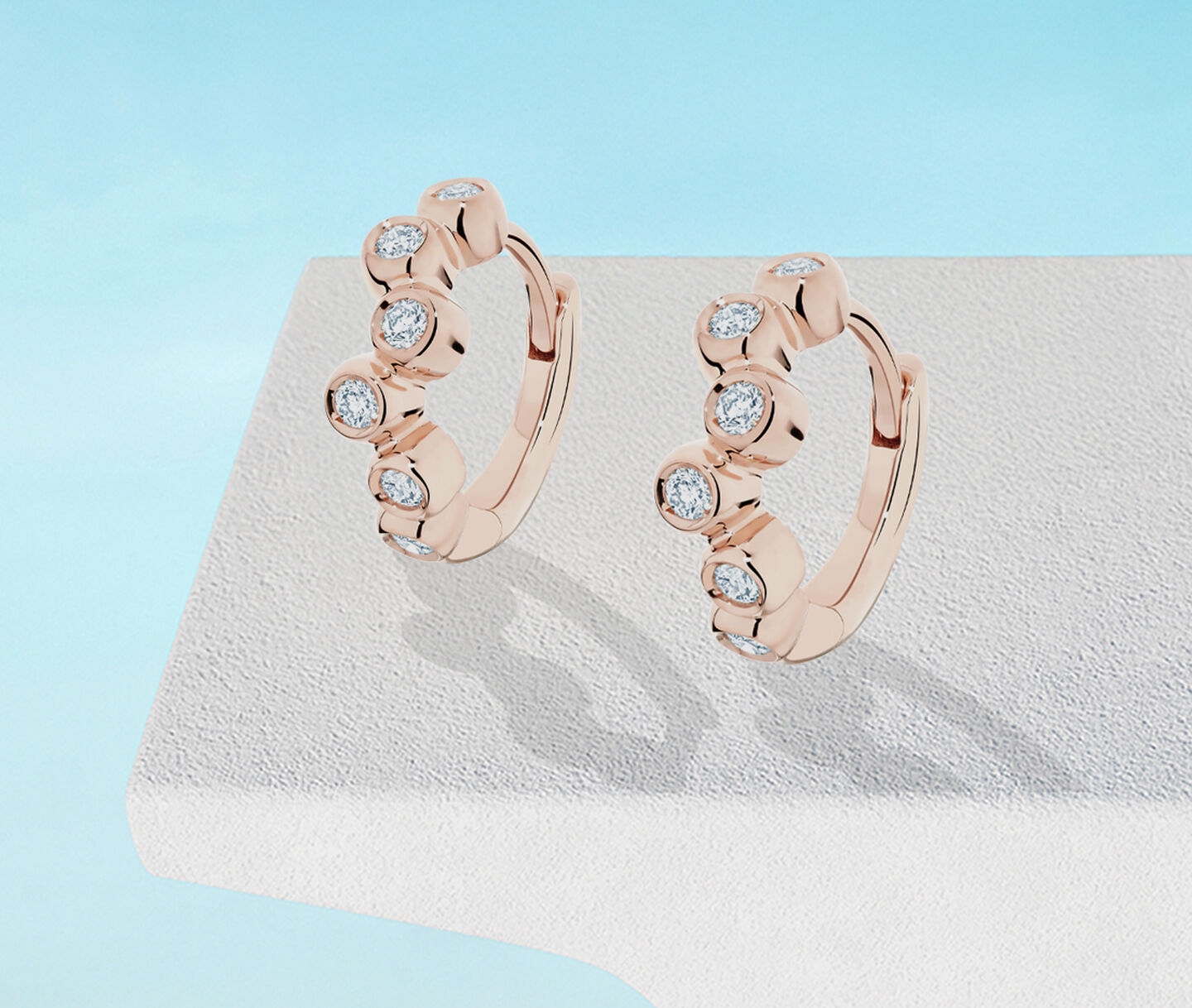 Birks Iconic Splash diamond and rose gold hoop earrings on a blue background.