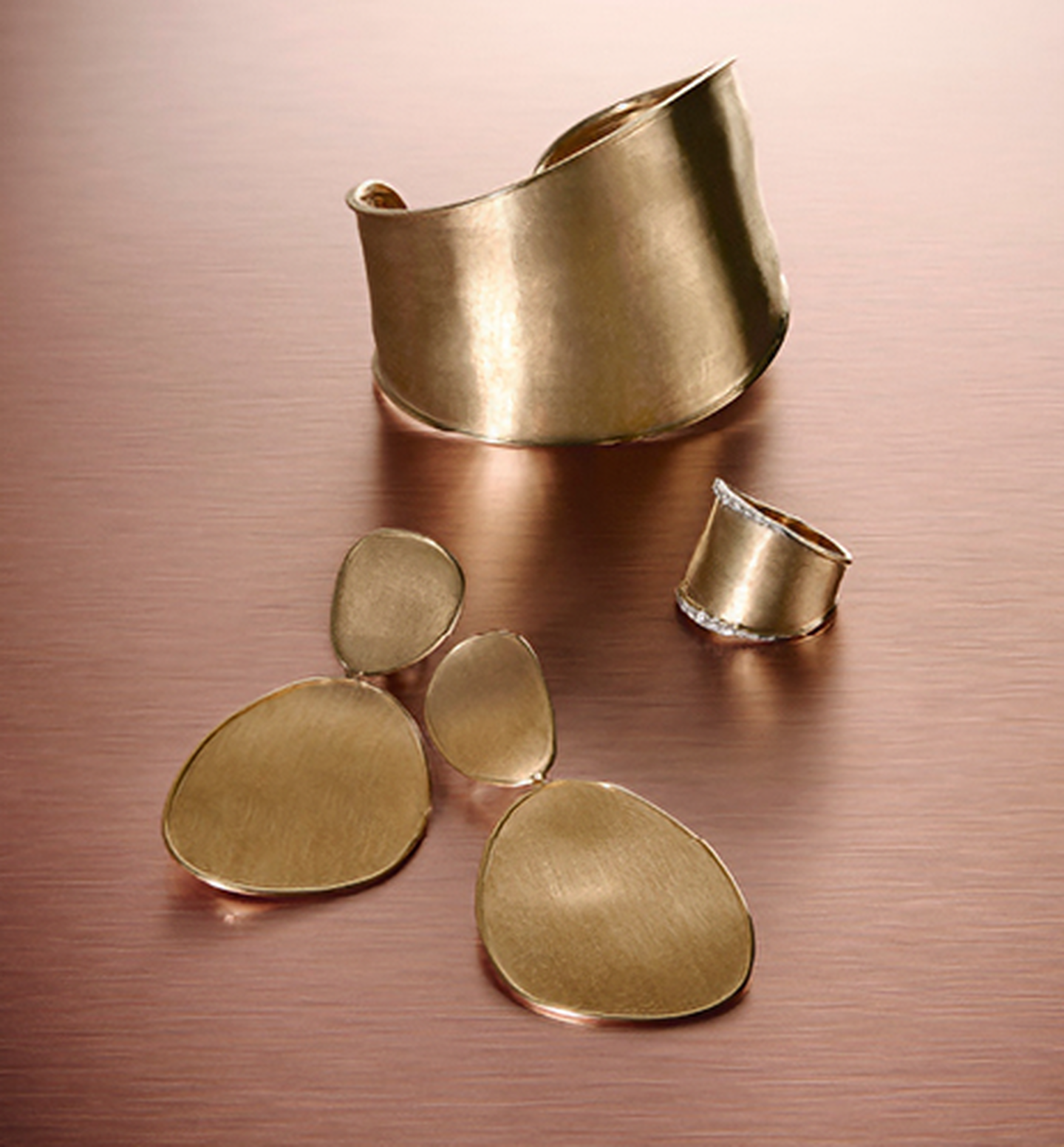 Marco Bicego Lunaria ring, earrings, and cuff bracelet on a pink background.