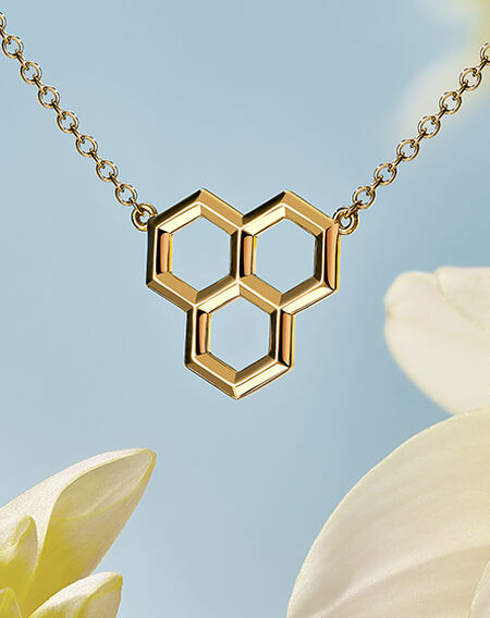 Birks Bee Chic gold honeycomb pendant on a blue sky and white daisy flower background.