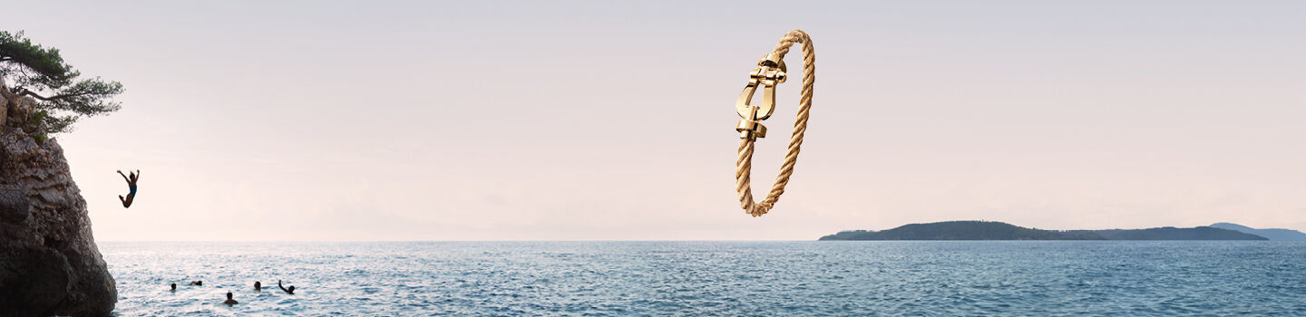 A FRED Force 10 gold bracelet on a background of a beach.
