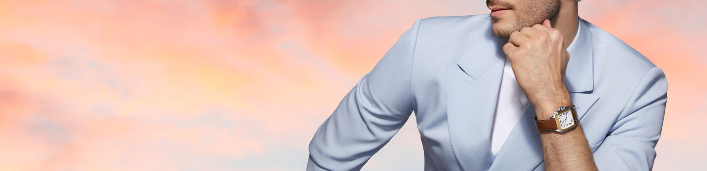 Man in a blue suit wearing a Cartier watch on a colourful background.