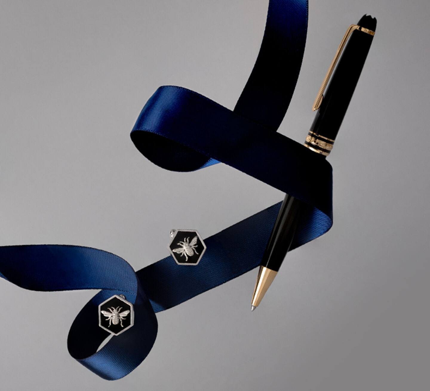 A black and gold pen beside a pair of black cuff links with a silver bee